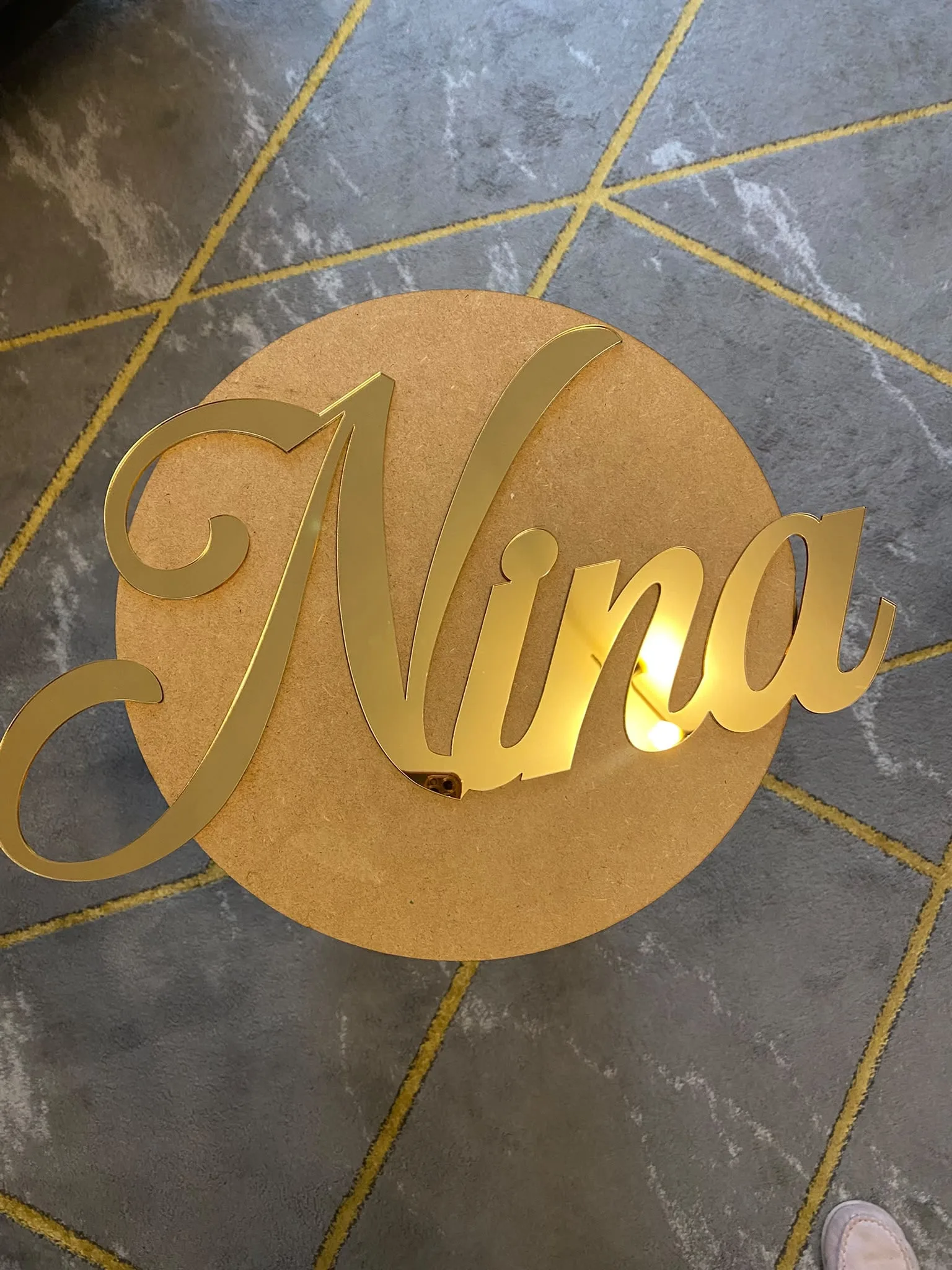 Ime „Nina“ od zlatnog pleksiglasa na okrugloj drvenoj podlozi