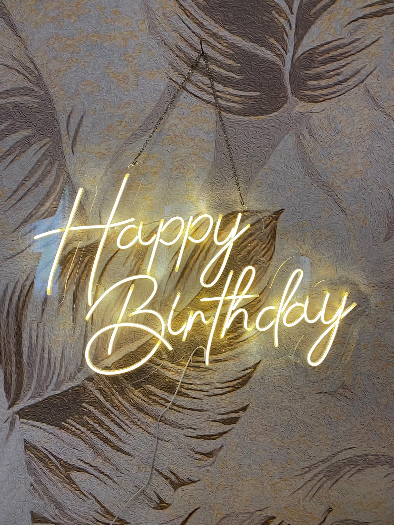Neonski natpis „Happy Birthday“ u toplom belom svetlu, na providnom pleksiglasu