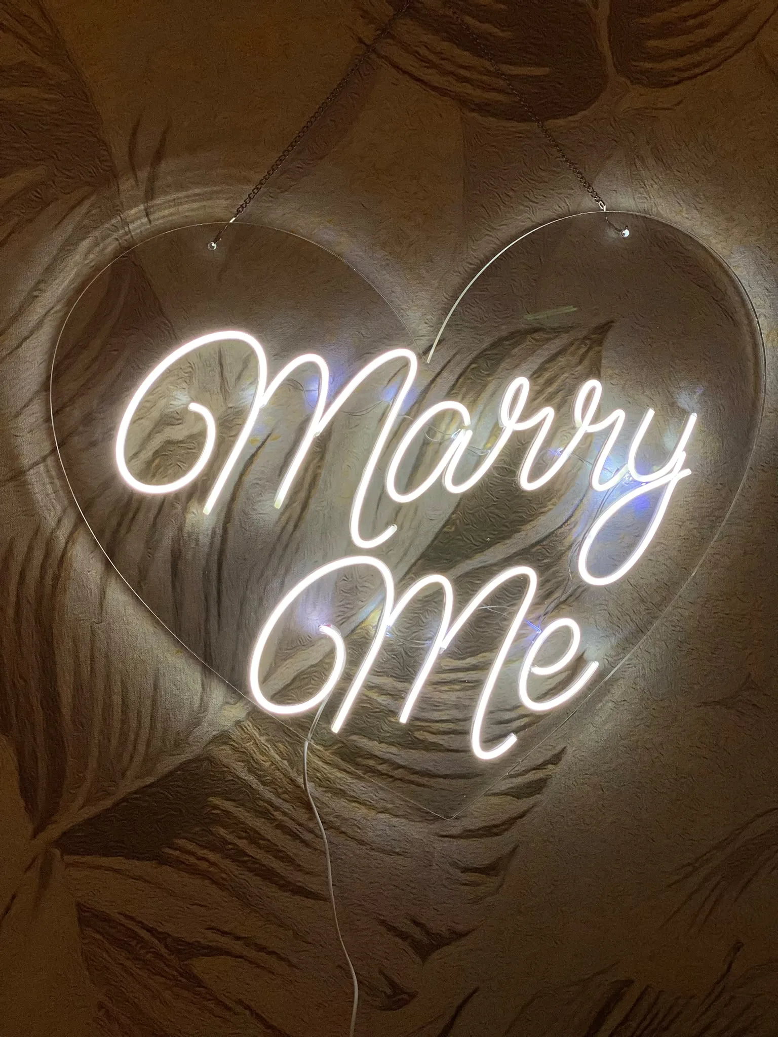 Neonski natpis „Marry Me“ u obliku srca, na providnom pleksiglasu